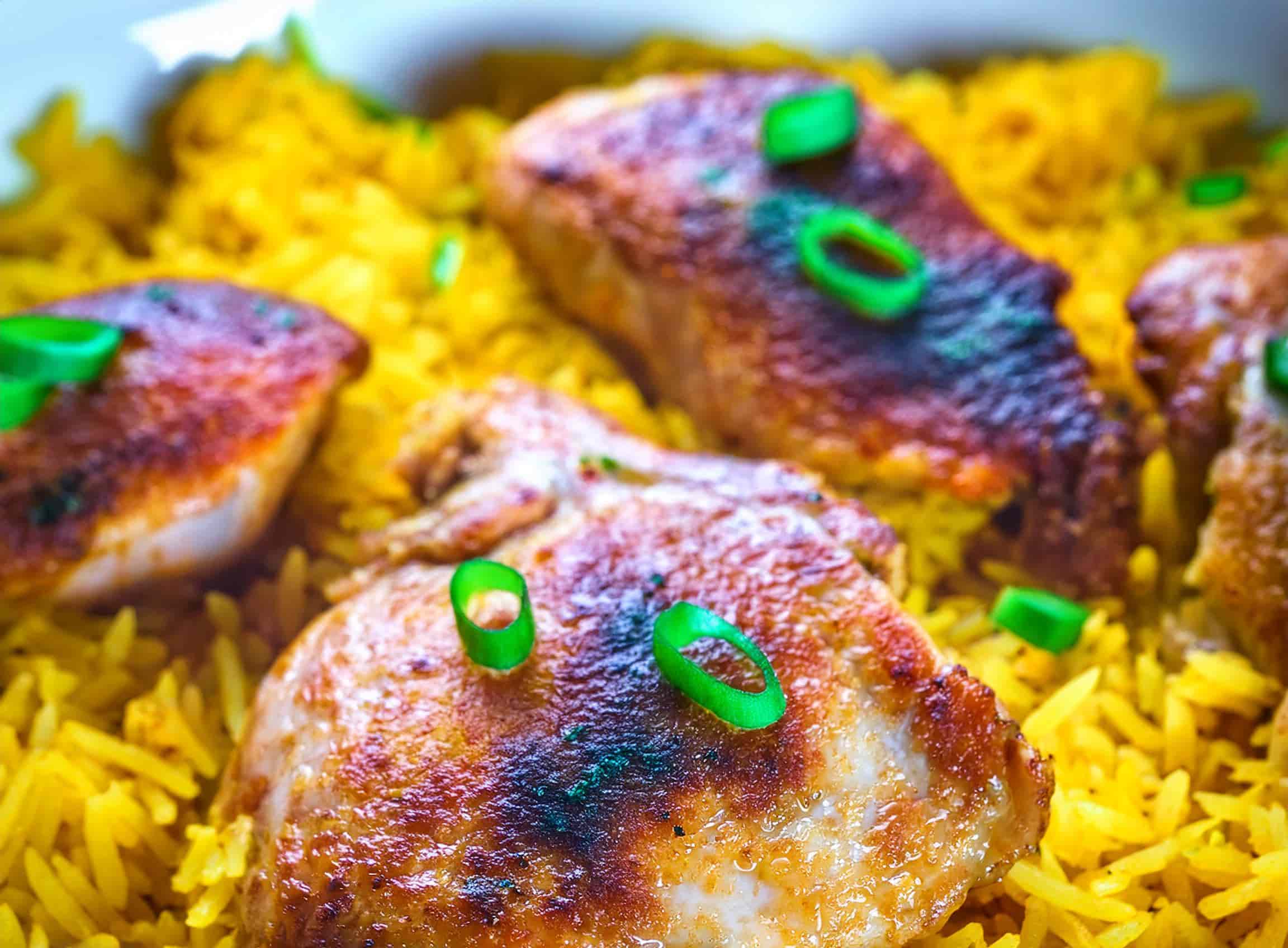 A hearty serving of Chicken and Yellow Rice Skillet on a white plate, featuring golden, flavorful rice and crispy chicken thighs.