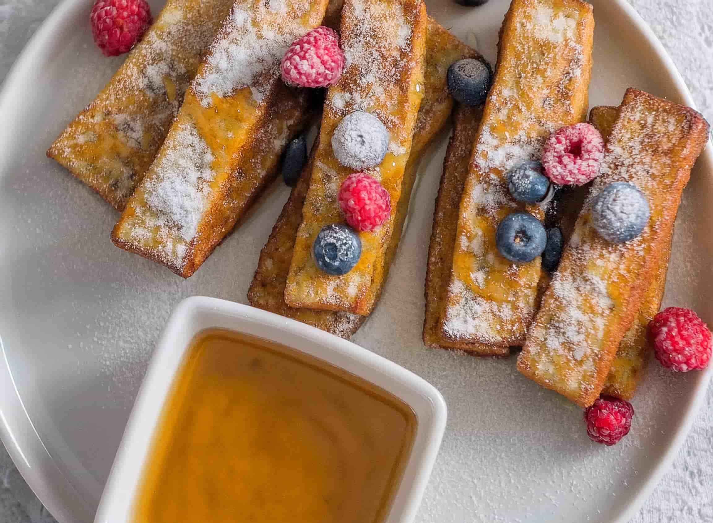 A plate of crispy frozen French toast sticks cooked in an air fryer served with maple syrup and fresh berries.