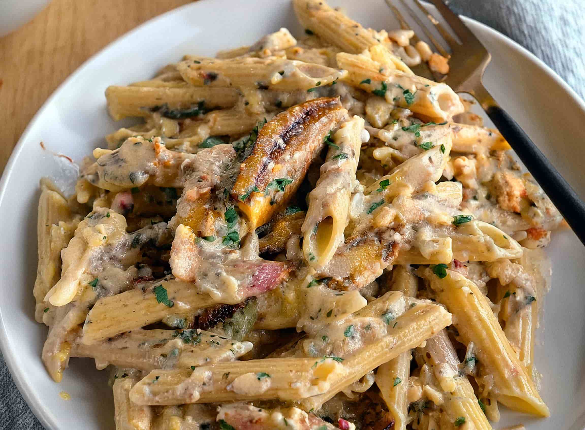 Garlic Parmesan Chicken Pasta being combined in a skillet with creamy sauce, tender chicken slices, and freshly chopped parsley
