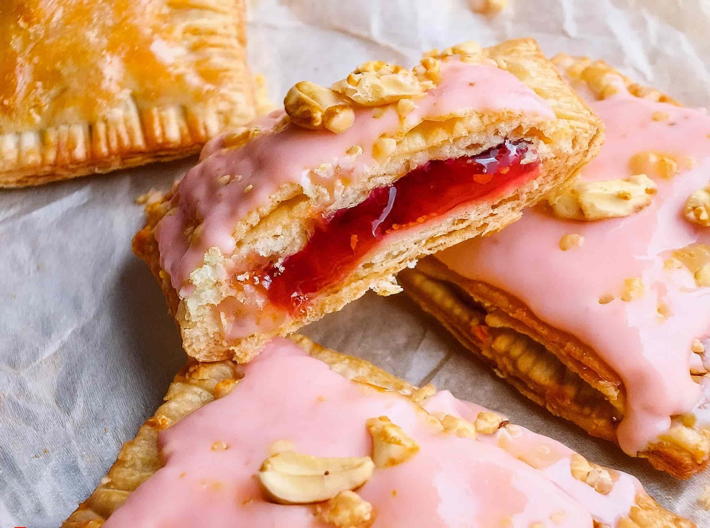 Homemade peanut butter and jelly Pop-Tarts with golden crusts and a glossy glaze, garnished with chopped peanuts and served on a rustic plate.