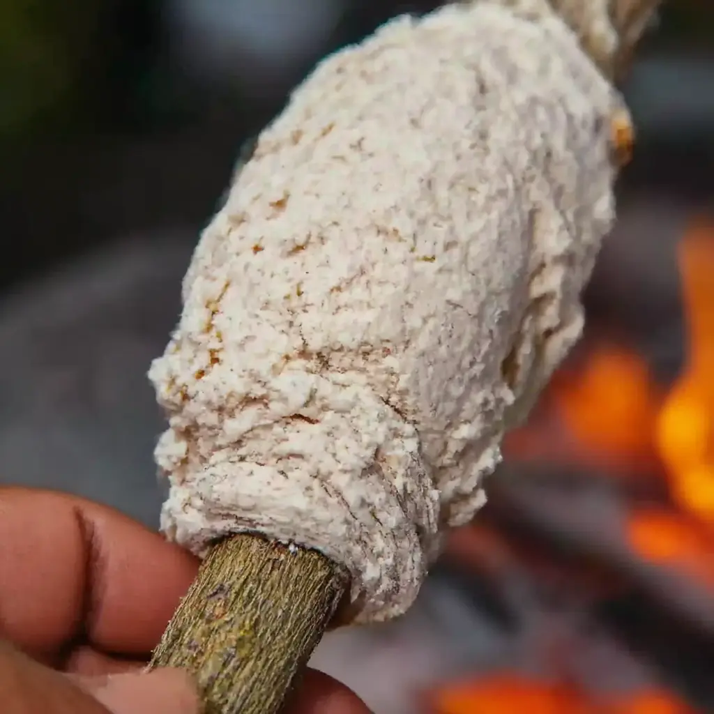 Hands wrapping bannock dough on a green stick